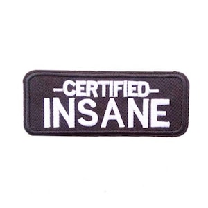 Puede incluir: Un parche rectangular negro con texto blanco que dice "-CERTIFIED- INSANE". El parche tiene un borde negro y probablemente está hecho de tela. El texto está en una fuente en negrita, sans-serif.