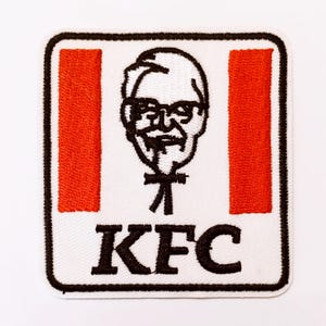 May include: Embroidered patch with the KFC logo. The design features a portrait of Colonel Sanders, red vertical stripes, and the letters "KFC" in black. The patch has a white background and a black border.