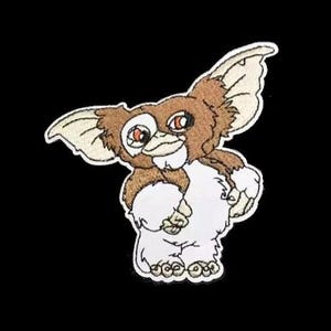 May include: Embroidered patch of a brown and white furry creature with large ears and red eyes. The creature is standing on its hind legs with its front paws raised.