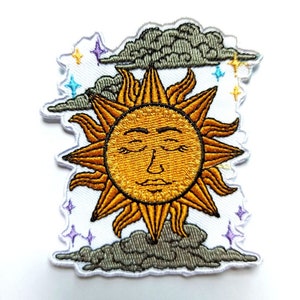 May include: Embroidered iron-on patch featuring a yellow sun with a closed-eye face, surrounded by grey clouds and purple, blue and yellow stars.