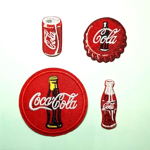 May include: Four embroidered patches featuring Coca-Cola branding. The patches include a red soda can, a red bottle cap, a red circle with a bottle design, and a red bottle. Each patch has white text that says "Coca-Cola" or "Cola".