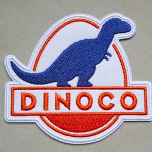 May include: Embroidered patch featuring a blue dinosaur silhouette on a white background. The patch has a red and white border, with the word "DINOCO" in orange letters at the bottom. The patch is likely for clothing or accessories.