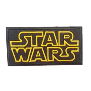 Może przedstawiać: Czarna naszywka haftowana z żółtym tekstem "STAR WARS" w pogrubionym, prostokątnym kroju.