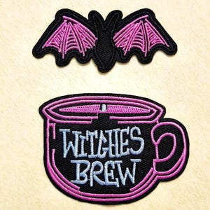 Puede incluir: Dos parches bordados que muestran un murciélago negro con alas rosas y una taza negra con borde rosa y el texto Witches Brew en letras azul claro. Los parches presentan costuras detalladas y contrastes de colores llamativos para su uso.