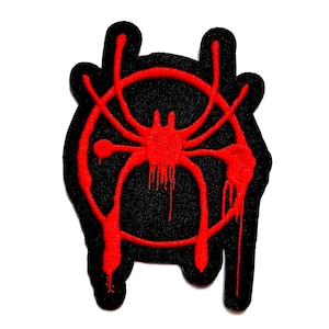 May include: A black embroidered patch featuring a vibrant red spider graphic centred within a circular frame. The design includes stylised paint drip effects extending from the spider legs and the circular border, creating a textured appearance.