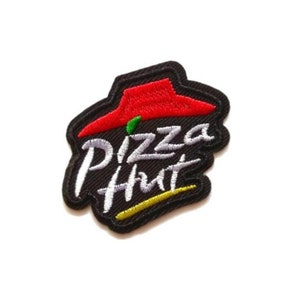 Puede incluir: Un parche bordado en negro, rojo, blanco y verde con las palabras "Pizza Hut" en una fuente blanca cursiva.