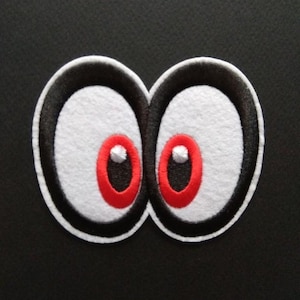 May include: Embroidered patch featuring a pair of cartoon eyes. The eyes have white irises, black outlines, and red pupils. The patch is on a black background, and the design is likely for clothing or accessories.