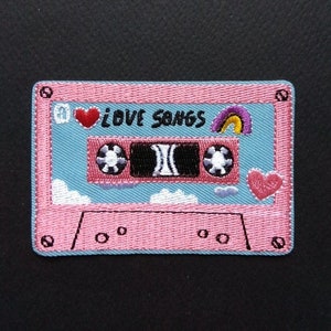 May include: Pink cassette tape patch with blue background. The tape has a rainbow, a heart, and the text "I LOVE SONGS".