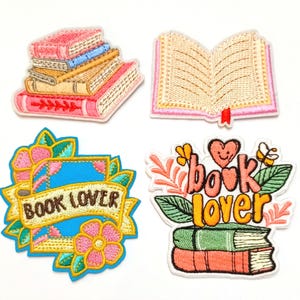 Puede incluir: Cuatro parches bordados con temática de libros. Uno muestra una pila de libros, otro un libro abierto con una cinta roja, y dos parches con las palabras "Book Lover" rodeadas de diseños florales. Los parches son de varios colores.