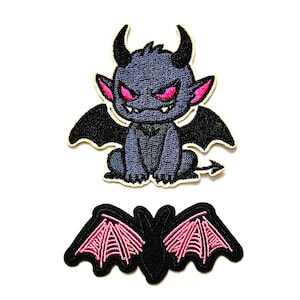 May include: Two embroidered patches. The top patch features a dark blue, horned creature with bright pink eyes and black wings. The bottom patch is a black silhouette of a bat with detailed, vibrant pink wing membranes and a pointed tail.