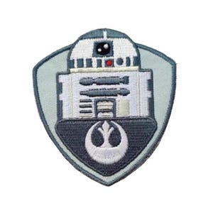 Op de afbeelding: Een geborduurde patch in grijs en wit met een robot met een Rebel Alliance-symbool. De robot heeft een wit lichaam met grijze details en een zwart oog. Het Rebel Alliance-symbool is wit op een grijze achtergrond.
