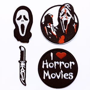 Op de afbeelding: Set van vier patches met horrorthema. Bevat een zwart-wit Ghostface-masker, een mes en twee ronde patches. Eén ronde patch heeft een Ghostface-ontwerp met rode bloedspetters en de andere zegt "I ❤️ Horror Movies."