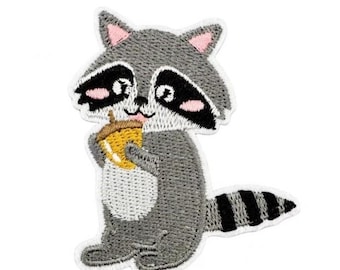 Puede incluir: Parche bordado para planchar de un mapache gris que sostiene una bellota amarilla. El mapache tiene ojos negros, una nariz rosa y una cola rayada de blanco y negro.