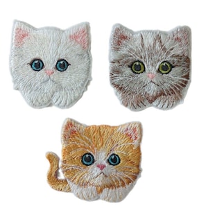 Könnte beinhalten: Drei gestickte Bügelbilder von Kätzchen. Ein weißes Kätzchen, ein braunes Tabby-Kätzchen und ein orangefarbenes Tabby-Kätzchen.