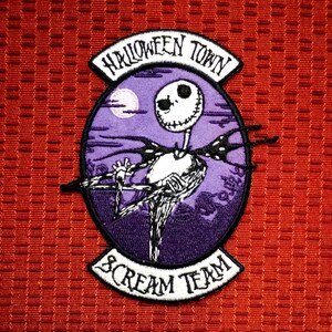 Könnte beinhalten: Gestickter Aufnäher mit Jack Skellington aus The Nightmare Before Christmas, vor einem lila Hintergrund mit Vollmond. Der Aufnäher trägt die Aufschrift "Halloween Town" und "Scream Team" in weißer Schrift.