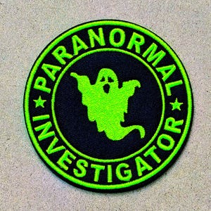 May include: A circular embroidered patch featuring a black background with a bright neon green border and a central neon green ghost graphic. The text PARANORMAL INVESTIGATOR is stitched in neon green capital letters around the ghost.