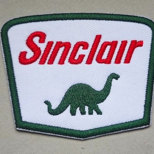 May include: A white patch with a green border, featuring the Sinclair logo. The logo is red text that reads "Sinclair" with a green dinosaur silhouette below it.