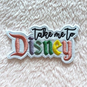 May include: White embroidered patch with the text "Take me to Disney" in black script. The word "Disney" is in rainbow colors with pink, purple, green, yellow, and orange.