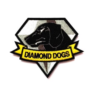 Könnte beinhalten: Ein rautenförmiger, bestickter Aufnäher mit der Silhouette eines schwarzen Hundes vor einem weiß-grauen Hintergrund. Ein gelbes Banner am unteren Rand enthält den schwarzen Schriftzug DIAMOND DOGS. Der Aufnäher hat einen dicken schwarzen Rand.