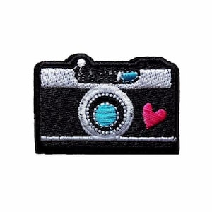 May include: Black and white embroidered iron-on patch of a camera with a blue lens and a red heart.