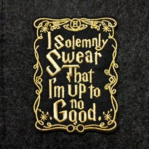 May include: Embroidered black patch with gold lettering and border. The text reads "I solemnly swear that I'm up to no good." The patch has a rectangular shape with rounded corners and is set against a dark gray fabric background.