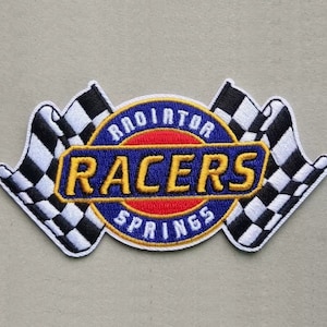 May include: An embroidered patch with a blue circle and the text "Radiator Springs Racers" in yellow. The circle is surrounded by two white and black checkered flags.