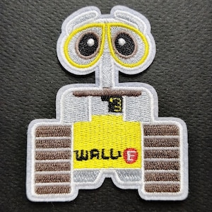 May include: An embroidered patch featuring the character WALL-E with large yellow-rimmed eyes, a grey body, brown treads, and a yellow chest panel displaying the text WALL-E in black letters with a red letter E, and a small number 3 on the top.