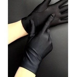 Puede incluir: Un par de guantes de satén negro. Los guantes son largos y llegan más allá de la muñeca. Los guantes son lisos y tienen una textura sedosa.