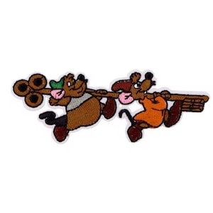 May include: An embroidered patch featuring two cartoon mice, one brown and one orange, carrying a long stick with a broom attached to the end. The brown mouse is wearing a green hat and the orange mouse is wearing a red hat.
