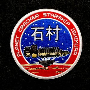 May include: Embroidered patch with a circular design. The patch features a red and white outer ring with the words "PLANET CRACKER STARSHIP ISHIMURA". The center has a blue background with white Japanese characters and a spaceship illustration.