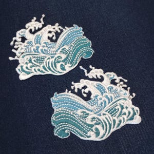 May include: Two embroidered patches featuring a stylized ocean wave design. The waves are depicted in shades of blue and teal with white detailing, set against a dark blue background. The patches are likely for clothing or craft projects.