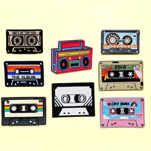 May include: A collection of eight embroidered patches featuring retro music themes, including a colorful boombox, various cassette tapes with labels like THE ALBUM, ROCK, and LOVE SONGS, and black and white designs on a light yellow background.