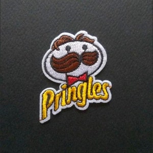 May include: Embroidered patch featuring the Pringles mascot with a white oval face, brown hair and mustache, and a red bow tie. The word "Pringles" is written in yellow with a white outline.
