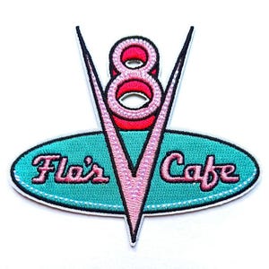 May include: Pink and red embroidered patch featuring a stylised 'V' shape with the number '8' inside. The 'V' is surrounded by a turquoise oval with the text 'Flair's Cafe' in pink.