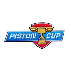 May include: An embroidered patch in blue and red with the words "Piston Cup" and a gold trophy with wings.