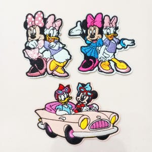 May include: Set of three embroidered patches featuring Minnie Mouse and Daisy Duck. One patch shows the pair hugging, another shows them arm in arm, and the third shows them in a pink convertible car. The patches have a white border.