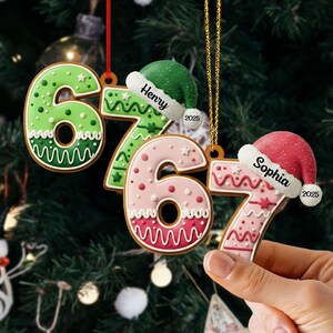 May include: Gingerbread-style Christmas ornaments shaped like the numbers 6 and 7, decorated with icing and festive details. Each ornament has a Santa hat with a name and the year 2025. One is held by a hand.