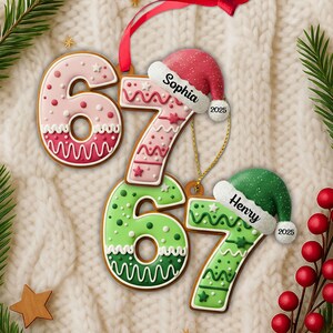 May include: Gingerbread-style Christmas ornaments shaped like the numbers 6 and 7. One ornament is pink with white and red details, the other is green with white details. Each has a Santa hat with a name and the year 2025.