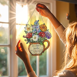 May include: A floral-themed hanging sign featuring a bouquet of colorful flowers in a decorative vase. The sign includes the text "Grandma's Garden" and names below. It is suspended by a silver chain.