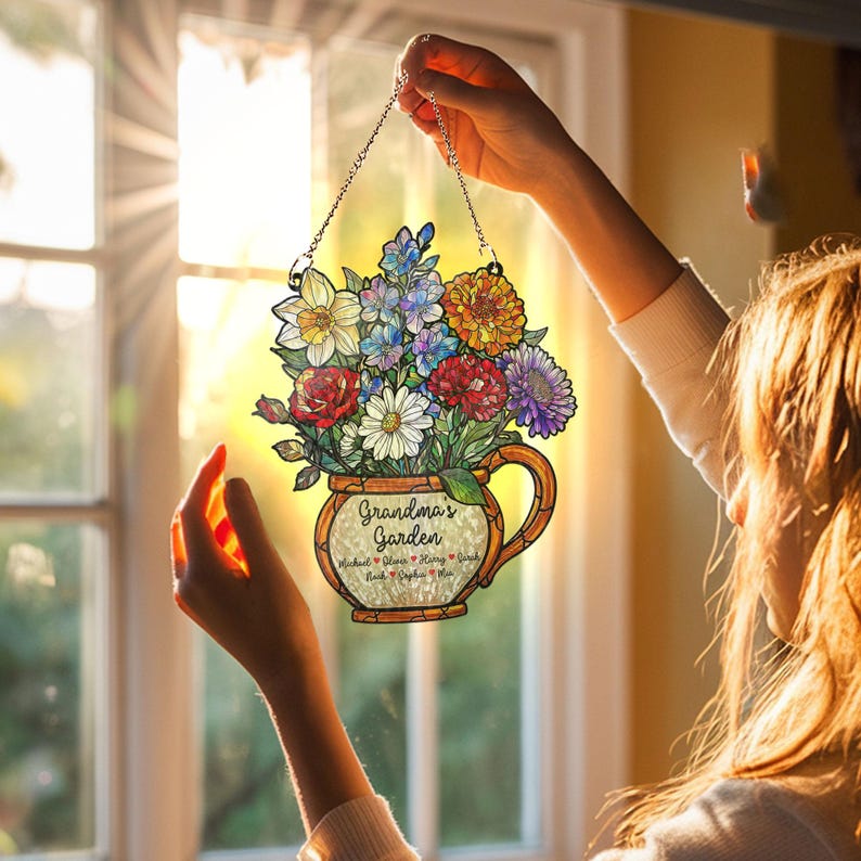 May include: A floral-themed hanging sign featuring a bouquet of colorful flowers in a decorative vase. The sign includes the text "Grandma's Garden" and names below. It is suspended by a silver chain.