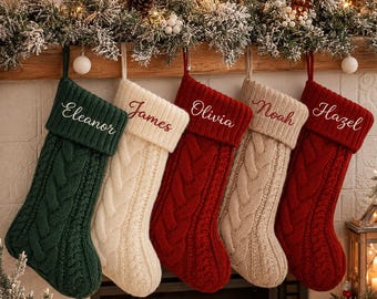 May include: Five cable-knit Christmas stockings hanging in a row. The first is dark green with the name Eleanor, the second is cream with James, the third is red with Olivia, the fourth is cream with Noah, and the fifth is red with Hazel.