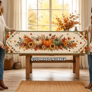 May include: A rectangular quilted table runner featuring a cream-colored background with a central autumn-themed print of pumpkins, sunflowers, and fall leaves. The border has a green and white checkered pattern with the text QUILT TABLE RUNNER.