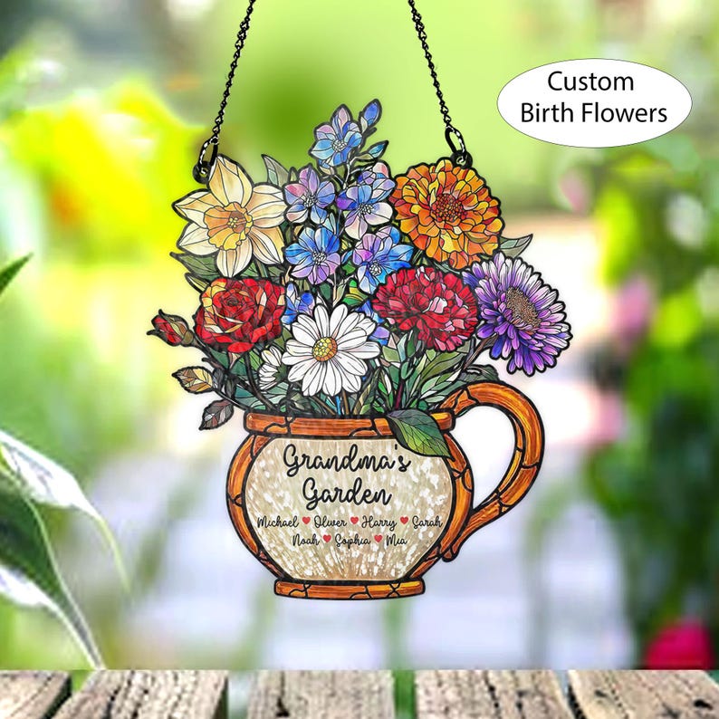 May include: A hanging floral decoration featuring a bouquet of colorful flowers in a decorative teacup-shaped vase. The text "Grandma's Garden" is displayed, along with names. The words "Custom Birth Flowers" are also visible.