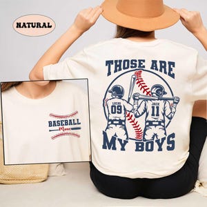 May include: A white t-shirt with the text "Those Are My Boys" and a baseball graphic with two baseball players. The players have the numbers 09 and 11 on their jerseys. The text "Baseball Mom" is on the front of the shirt.
