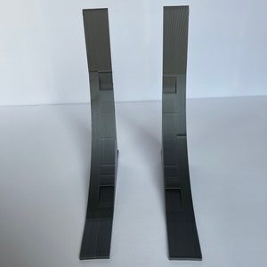 May include: Two gray 3D printed corner brackets. The brackets are curved and have a textured surface.