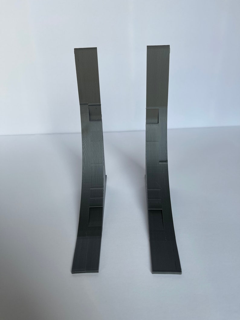 May include: Two gray 3D printed corner brackets. The brackets are curved and have a textured surface.