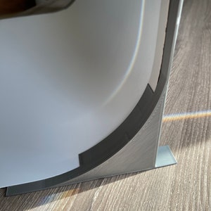 May include: A close-up of a gray plastic corner brace with a curved edge. The brace is attached to a white surface and is resting on a wood floor.