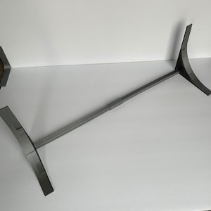May include: A gray metal stand with two adjustable legs. The stand is designed to hold a large object, such as a TV or monitor.