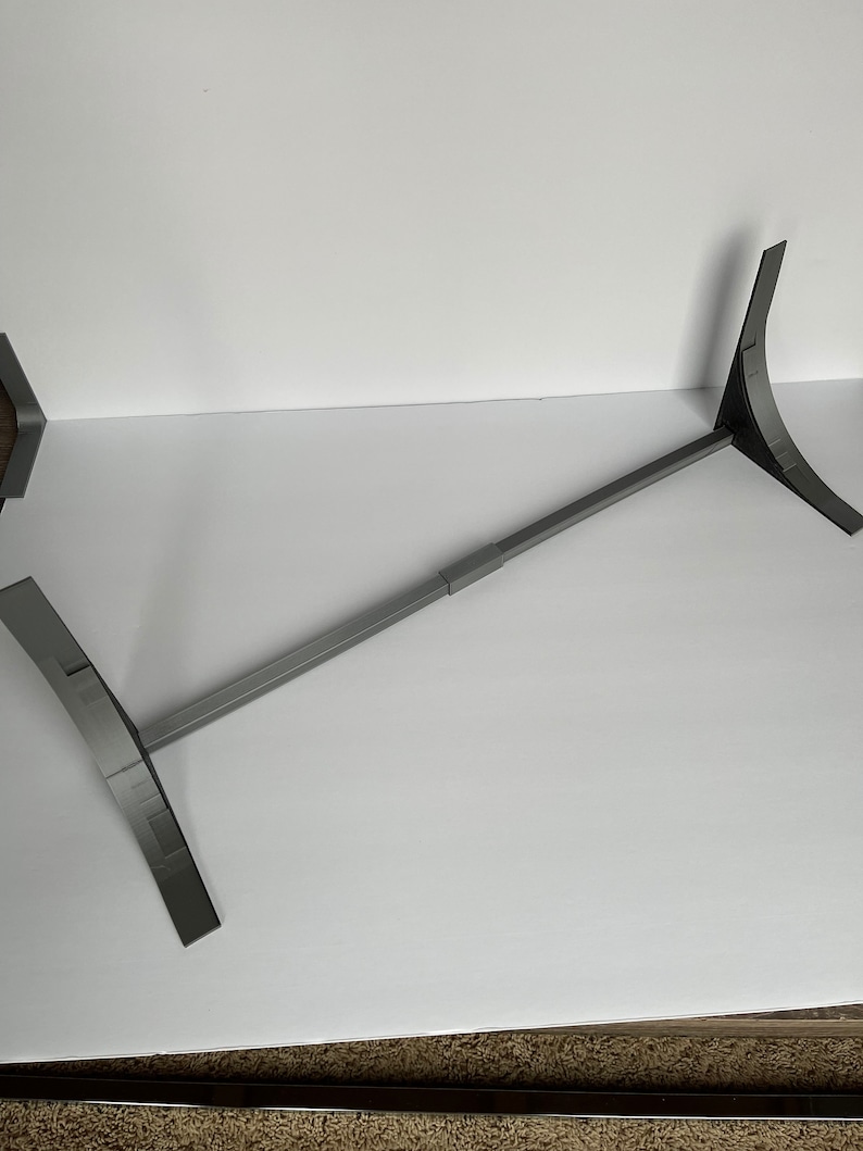 May include: A gray metal stand with two adjustable legs. The stand is designed to hold a large object, such as a TV or monitor.