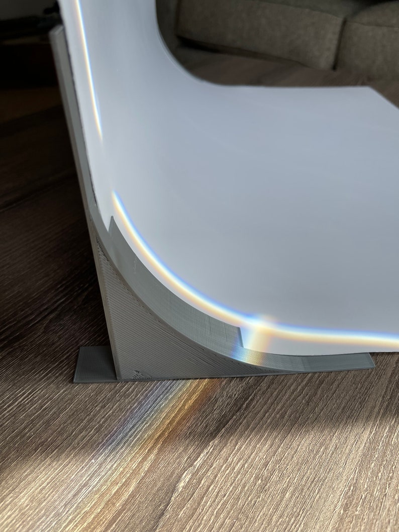 May include: A gray, curved backdrop stand with a white backdrop. The stand has a base with a rectangular shape and a curved support for the backdrop. The backdrop is slightly curved and has a slight sheen.